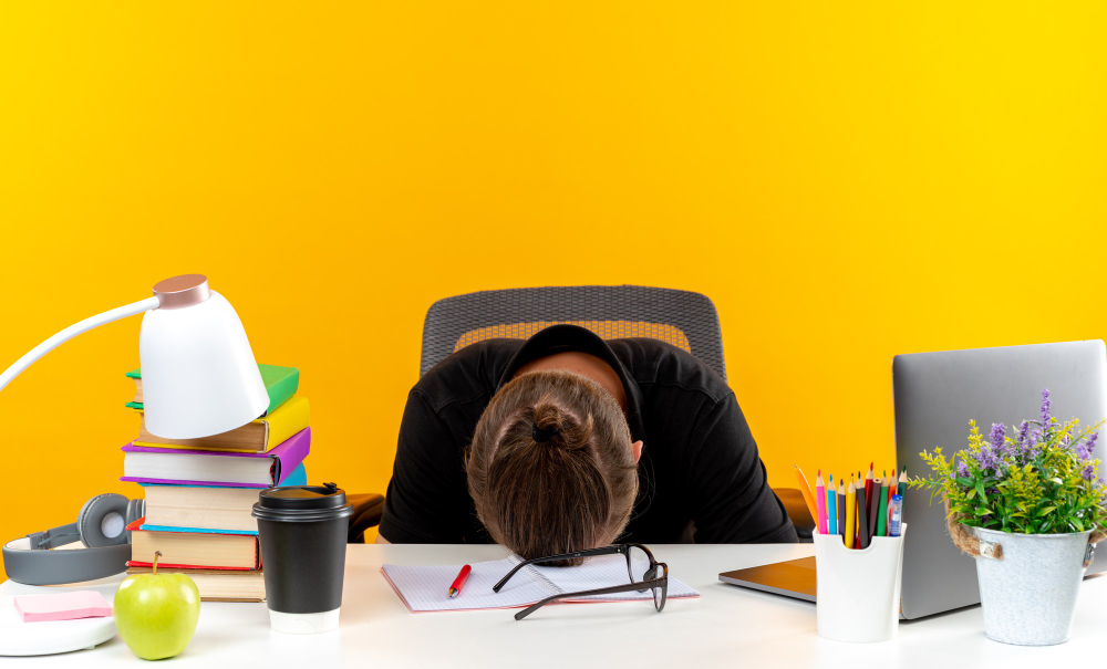 young guy student sitting table with school tools lowered head table isolated orange wall