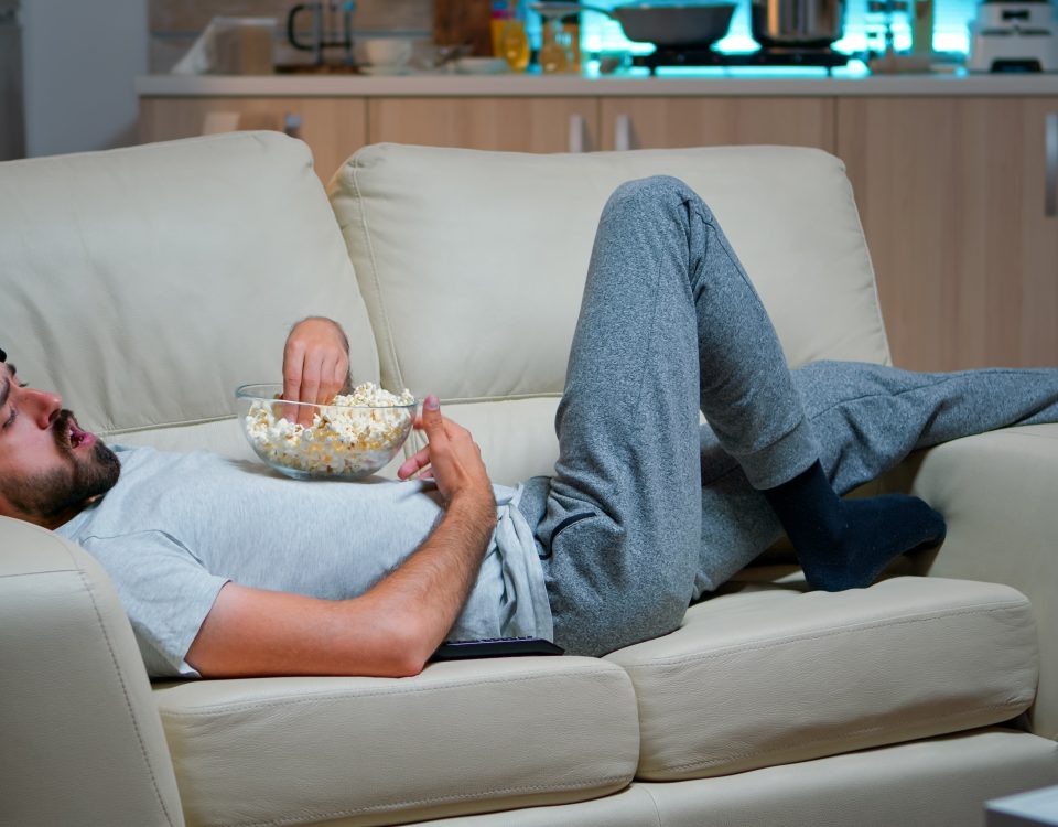 man lying sofa eating popcron watching tv